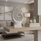 A modern abstract white sculpture on a rectangular base, displayed on a light wood floating shelf in a contemporary living room setting.