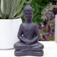 A terracotta Buddha figurine in a weathered finish, displayed in a garden setting.