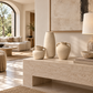 Three textured beige ceramic vases of different heights and shapes displayed on a light stone console table in a modern, sunlit living room.