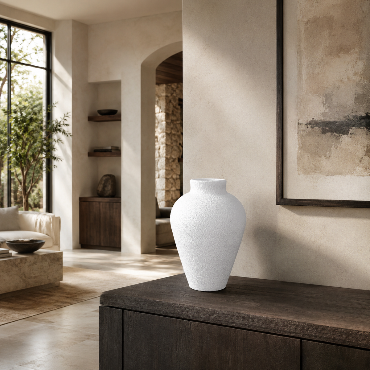 A textured white ceramic vase with a wide bulbous body and narrow neck, displayed on a dark wood console table in a modern, sunlit minimalist living room.