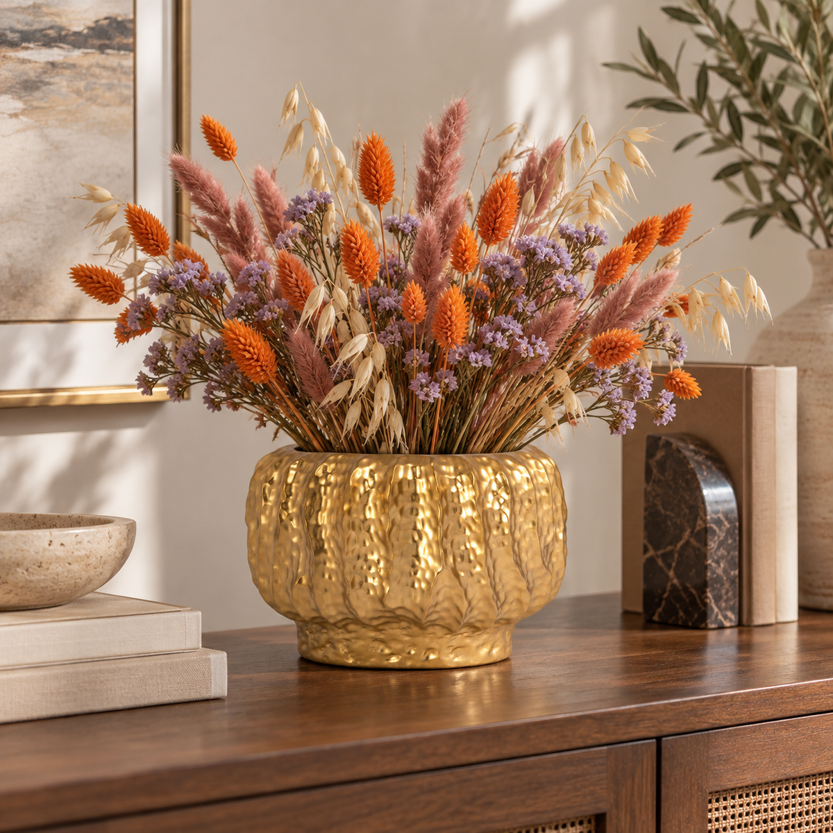 A textured gold ceramic vase filled with dried orange, pink, and purple flowers, styled on a dark wood console table in a warm, modern interior setting.