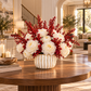 A floral arrangement of white peonies and red berries in a ribbed cream ceramic vase, displayed on a round wooden table in a bright, upscale living room.