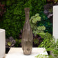 A ceramic vase with a distressed finish in silver color, displayed against a plant backdrop.