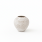 A small round ceramic vase with a textured, speckled finish in a light beige and gray color, set against a solid white background.