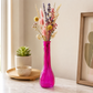 A bright magenta pink glass vase filled with dried flowers, set on a marble countertop in a styled home interior next to a small potted succulent and a framed print.