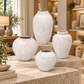 Four textured ceramic vases in varying sizes arranged on stone pedestals inside a warm, modern home decor showroom.